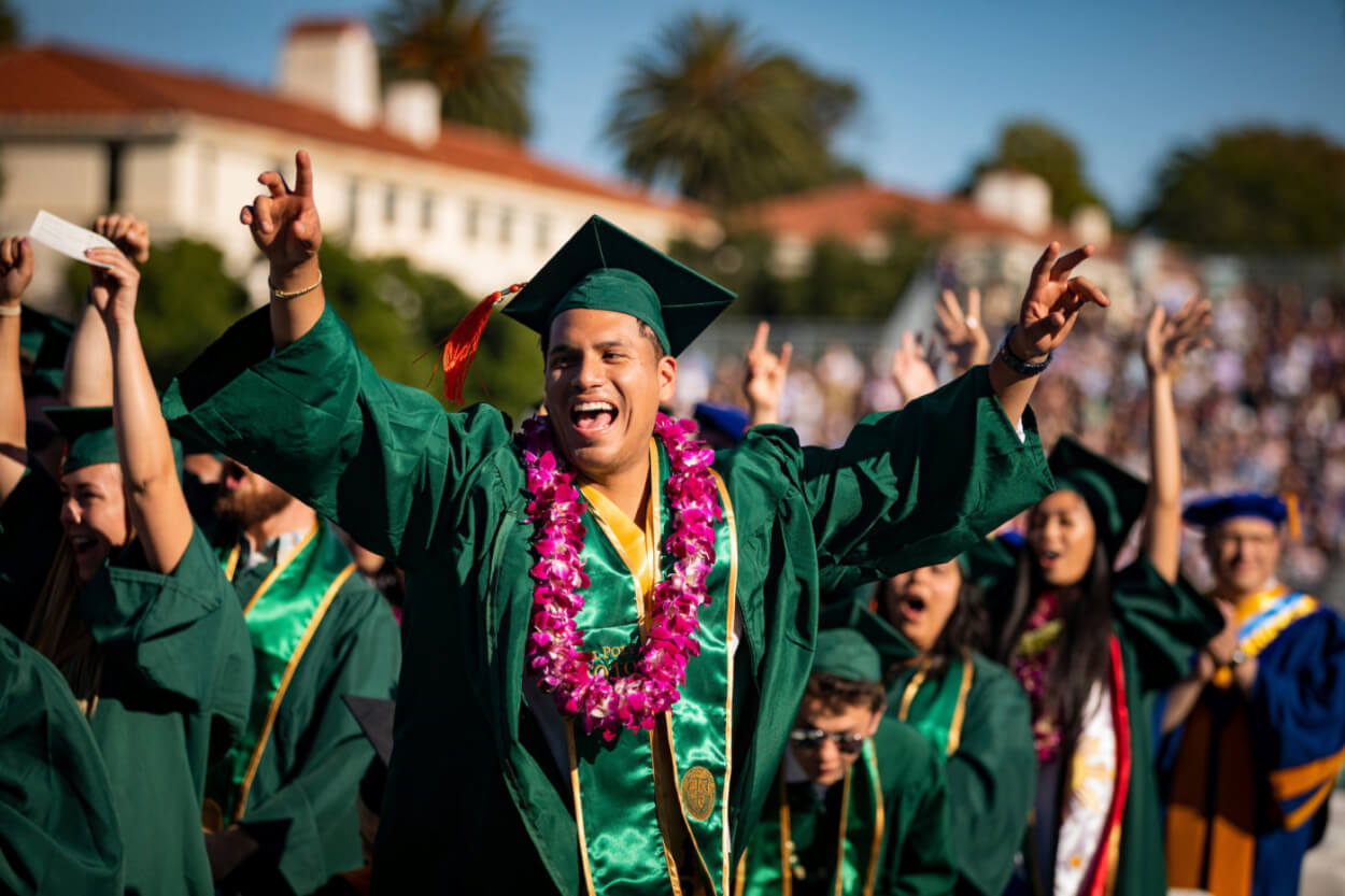 A graduating student wearing regalia and cheering during the Cal Poly Commencement ceremony