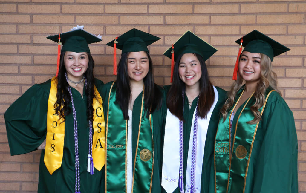 A portrait of four graduating students wearing regalia and smiling